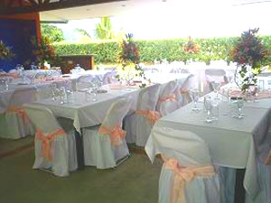 A dining room set up very formally with white table and chair cloths. 