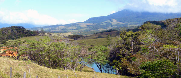 The large pond is here glimpsed through the trees and in the distance appears the cloud-topped Tenorio Volcano. 