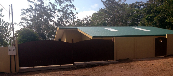 The newly constructed home hides behind a tall fence on a quiet lane.