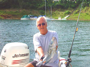 A fisherman in a small boat hold a large rainbow bass in front of the marina