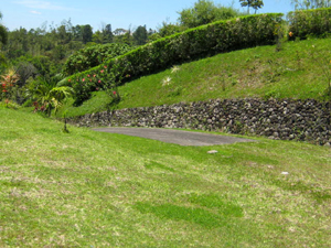 The paved driveway leads to the large flat lot with a natural stone retaining wall stretching lengthily behind it.