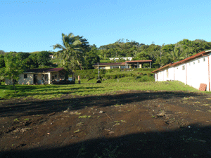 Looking from the plantel back toward the Chimurria road, one sees neighbors on left and right of the lot entrance and on the hill across the road. 