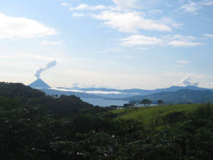 The Arenal Volcano, looking smaller than actuality because of the camera setting, illustrates its active nature with a tall plume of smoke.